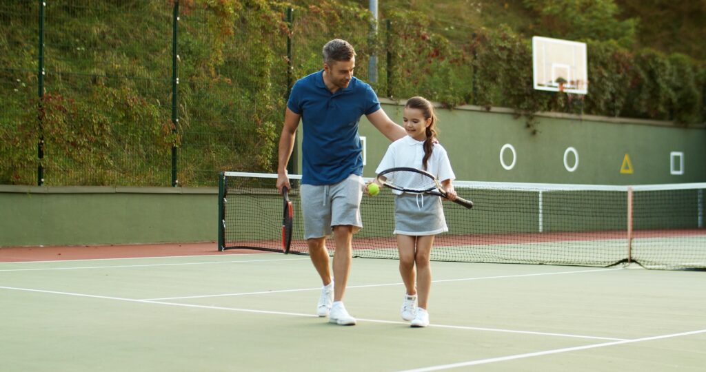 father motivating daughter on tennis court. Teaching her lessons to fight her own battles